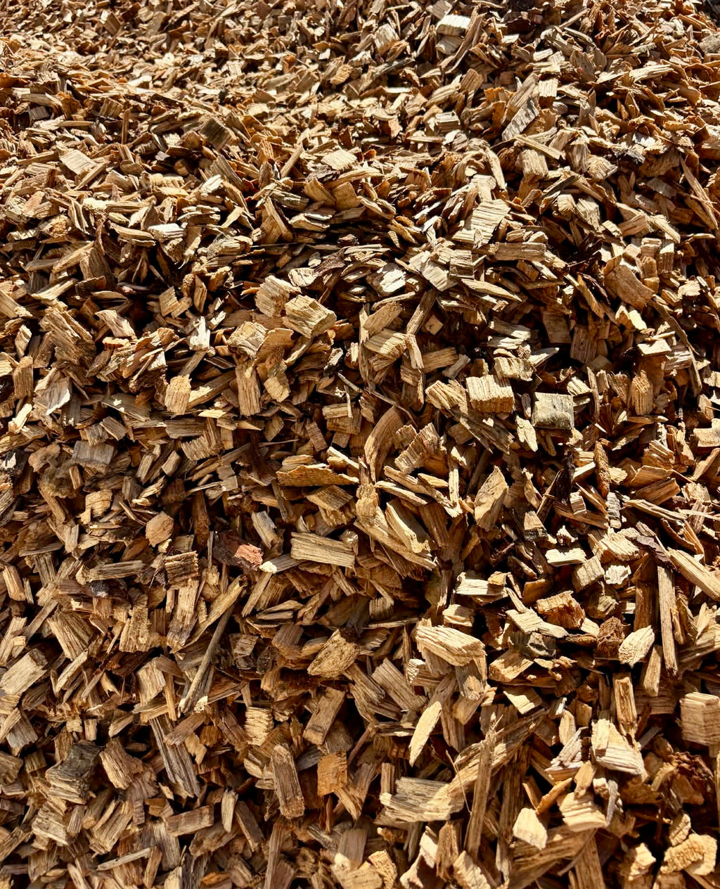 A close-up view of a large pile of natural wood chips and bark mulch, showing textured brown and tan wood pieces filling the frame.