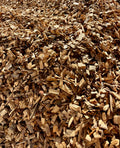 A close-up view of a large pile of natural wood chips and bark mulch, showing textured brown and tan wood pieces filling the frame.
