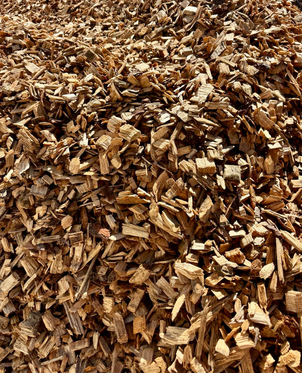 A close-up view of a large pile of natural wood chips and bark mulch, showing textured brown and tan wood pieces filling the frame.