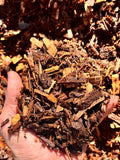 A close-up of a hand holding a mixture of dried leaves, bark, and small brown organic pieces against a background of the same material.
